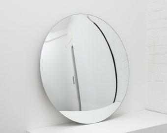 May include: A round, silver-framed mirror reflecting a white room with a door.