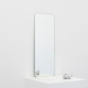 May include: A silver snail sculpture sits on a white surface in front of a large, rectangular mirror with rounded edges.