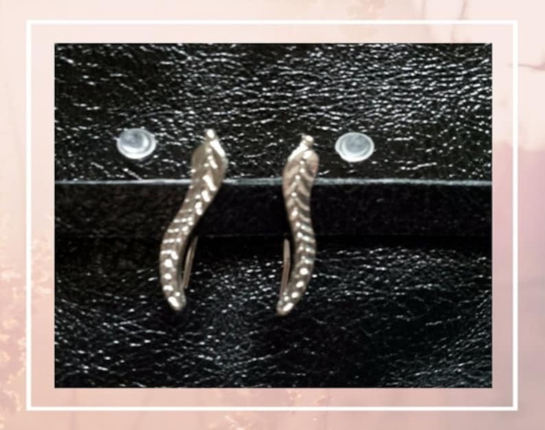 May include: A pair of silver earrings with a leaf design. The earrings are on a black background.