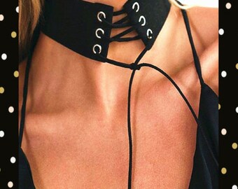 May include: Black choker necklace with a wide band and silver-tone grommets. The choker features a lace-up design in the front and thin straps that tie in the back. The necklace is made of a soft, suede-like material.