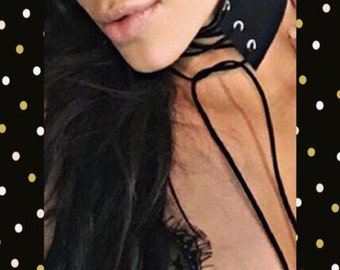 May include: A black leather choker necklace with a lace-up design and silver eyelets. The necklace is tied in a bow at the front.
