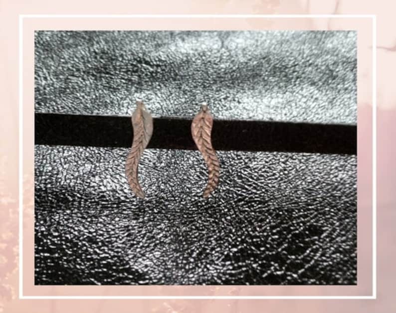 May include: A pair of silver feather earrings. The earrings are small and delicate, and they have a simple, elegant design.