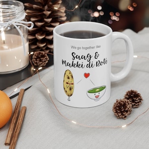 May include: White ceramic mug with a black and white illustration of a roti and a bowl of saag. The text on the mug reads "We go together like Saag & Makki di Roti".