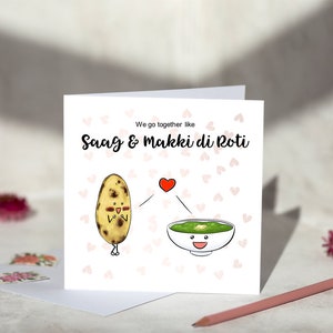 May include: A greeting card featuring a cartoon illustration of a roti and a bowl of saag. The text on the card reads "We go together like Saag & Makki di Roti".