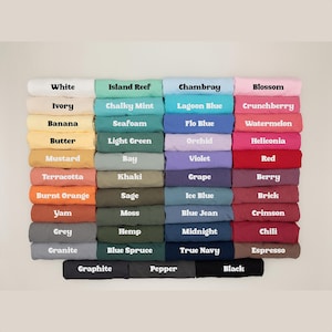 Pu&ograve; includere: Un'esposizione di tessuti piegati in vari colori, ciascuno etichettato con il nome del colore corrispondente. I colori includono bianco, avorio, banana, burro, senape, terracotta, arancione bruciato, igname, grigio e granito.