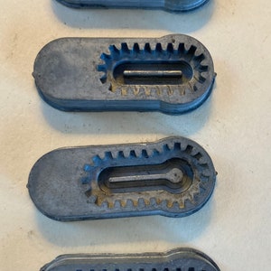 May include: Four gray plastic pieces with a gear-like design around the edge and a slot in the center. The pieces are arranged vertically, with the top piece being the largest and the bottom piece being the smallest.