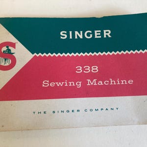 May include: Vintage Singer 338 Sewing Machine instruction manual. The cover features a teal and pink color scheme with the Singer logo and the text "338 Sewing Machine". The Singer Company is printed at the bottom.