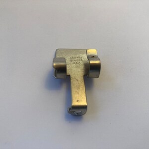 May include: A silver metal sewing machine part with the text "183845 SINGER U.S.A." on it.