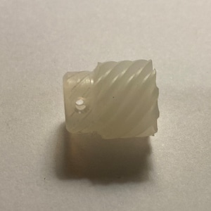 May include: A white plastic gear with a spiral design. The gear has a small hole in the center.