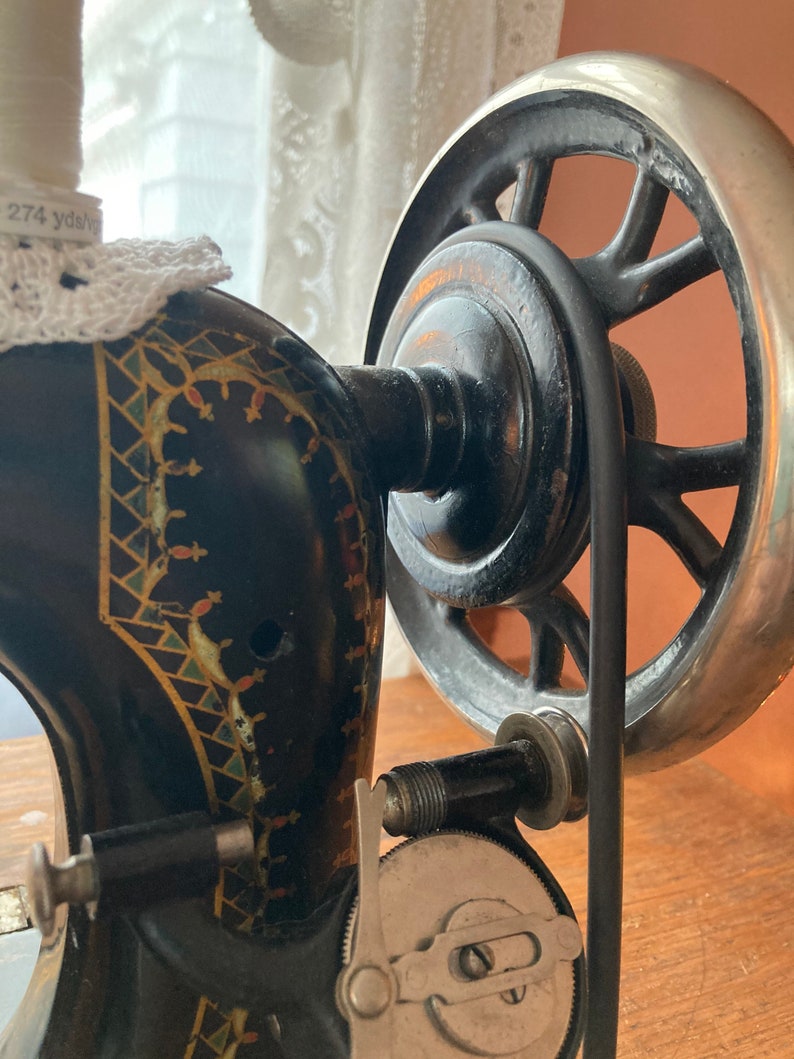 May include: A vintage black sewing machine with a decorative floral design. The machine has a large silver wheel and a spool of thread with a label that reads "274 yds".