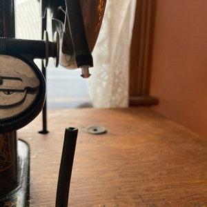 May include: Close-up of a vintage sewing machine with a black metal body and a silver dial. The machine is on a wooden table.