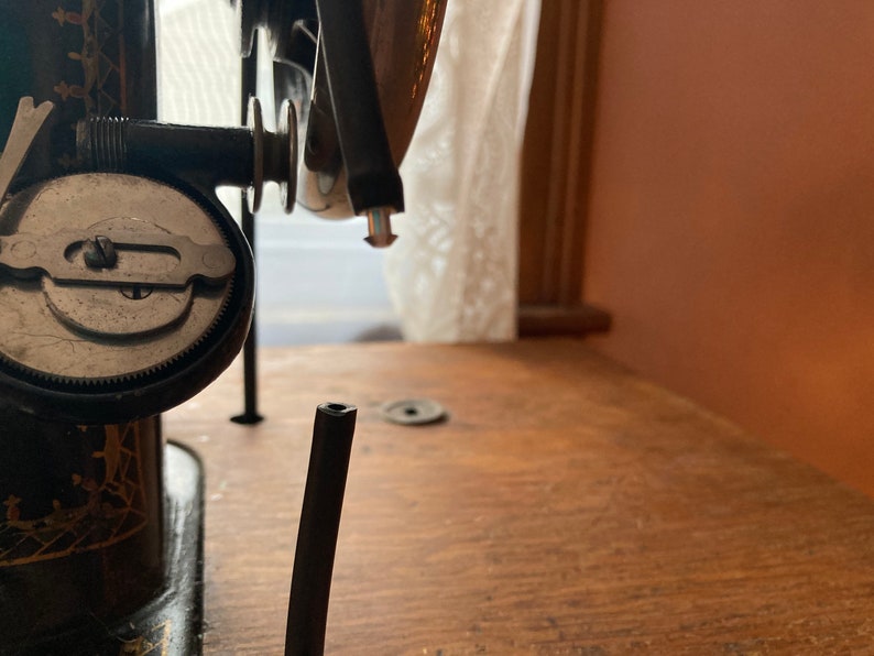 May include: Close-up of a vintage sewing machine with a black metal body and a silver dial. The machine is on a wooden table.