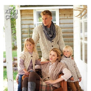 Puede incluir: Una familia con suéteres de punto posa para una foto. Los suéteres son de varios tonos de crema y marrón. El texto "Aran Book 1 Stylish knits for all the family by SUE BATLEY-KYLE" está en la parte inferior de la imagen.