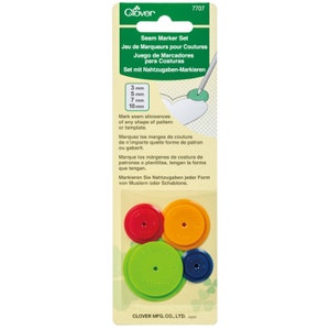 May include: A set of four colourful plastic seam marking tools. The tools are in red, orange, green, and blue. The tools are circular and have different sizes: 3 mm, 5 mm, 7 mm, and 10 mm. The tools are packaged on a white card with green and white text. The text reads: "Seam Marker Set, Jeu de Marqueurs pour Coutures, Juego de Marcadores para Costuras, Set mit Nahtzugaben-Markieren".