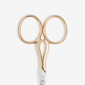 May include: Gold-toned small scissors with a silver blade. The scissors have a classic design with a curved handle.