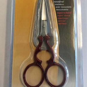 May include: Red embroidery scissors with a silver blade and a 90 mm length. The packaging features the text "Stickschere" and "Embroidery scissors".