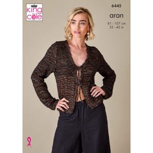 Può includere: Cardigan lavorato a maglia Aran marrone con scollo a V e chiusura con lacci. Il cardigan ha maniche lunghe e un aspetto strutturato. L'immagine include il testo "aran" e misure di 81-107 cm.