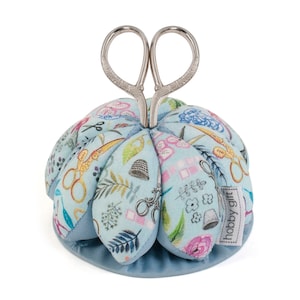 May include: A blue pincushion with a floral pattern featuring sewing-themed illustrations. The pincushion has a silver pair of scissors attached to the top.