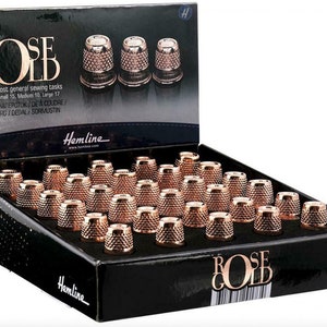 Op de afbeelding: Een doos met 36 naalden in roosgoud in drie maten: klein, middel en groot. De doos is zwart met witte tekst die "Rose Gold" en "Hemline" luidt.