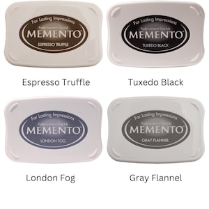 Pode incluir: Quatro almofadas de tinta para carimbar, cada uma com uma cor diferente. As almofadas de tinta s&atilde;o etiquetadas como "Espresso Truffle", "Tuxedo Black", "London Fog" e "Gray Flannel". Cada almofada de tinta tem as palavras "For Lasting Impressions" e "Fade-resistant Dye Ink" impressas nela, juntamente com a palavra "MEMENTO" em uma fonte estilizada.