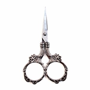 May include: Antique silver-toned scissors with ornate floral details on the handles. The blades are sharp and pointed.