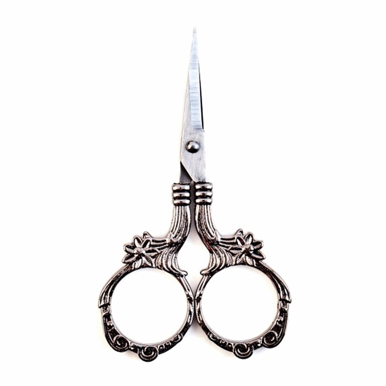 May include: Antique silver-toned scissors with ornate floral details on the handles. The blades are sharp and pointed.