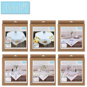 May include: A collection of six cross-stitch tablecloth kits in brown cardboard packaging. Each kit features a different floral design, including roses, sunflowers, and other flowers. The kits are labeled "Cross Stitch Tablecloth Kit" and include the brand name "Trimits".