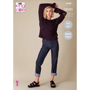 Può includere: Una donna indossa un maglione lavorato a maglia aran bordeaux scuro con maniche a raglan e jeans blu scuro. Il maglione ha un aspetto strutturato. L'immagine include il testo "Easy Knit" e "Raglan Sleeve". La lunghezza del maglione è di 81-107 cm.