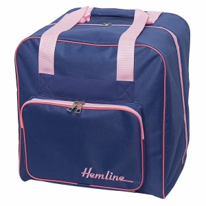 May include: A navy blue sewing machine carrying case with pink accents. The bag has pink handles, trim, and a front pocket with a zipper. The word "Hemline" is embroidered in pink on the front. The bag is designed to carry sewing machines and supplies.