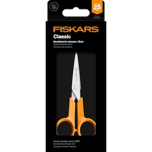 May include: Orange-handled Fiskars Classic needlework scissors, 13cm, in a black package. The scissors have silver blades and the package includes the text "FISKARS Classic" and "25 years de garantie". The package also states "Iconic design since 1967".