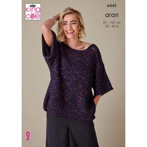 Può includere: Un maglione lavorato a maglia blu scuro, rosso e viola con scollo a barchetta e maniche corte. Il maglione è indossato da una persona. Il testo "6443 aran" e le misure di 81-107 cm (32-42 in) sono visibili.