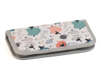 Puede incluir: Una funda gris con cremallera con fondo blanco y un patrón de ovejas negras que sostienen ovillos de lana de varios colores. El texto "stitch happy" está impreso en la funda.