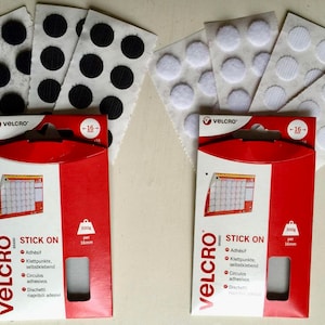 May include: Two packs of Velcro brand stick-on fasteners. Each pack contains 16 white or black round adhesive dots. The packaging is red with white text that says "VELCRO STICK ON" and "300g per 16mm".