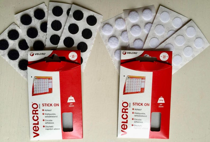 May include: Two packages of Velcro brand stick-on fasteners. Each package contains 16 white or black round adhesive dots. The packaging is red with white text that says "VELCRO STICK ON" and "300g per 16mm".