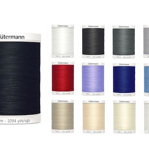 Op de afbeelding: Een verzameling van 12 spoelen Gütermann garen in verschillende kleuren, waaronder zwart, wit, rood, blauw, grijs en beige. Elke spoel bevat 1000 meter (1094 yards) garen.