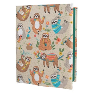 Op de afbeelding: Een beige stoffen notitieboekomslag met een groene rug. De omslag heeft een herhalend patroon van luiaards in verschillende poses, die hoeden, sjaals dragen en garenbollen vasthouden. Sommige luiaards houden lichtjes vast en andere dragen truien.