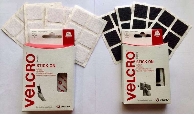 May include: Two packages of Velcro brand stick-on squares. The package on the left contains white squares and the package on the right contains black squares. Both packages have the text "STICK ON" and "VELCRO BRAND" printed on them.