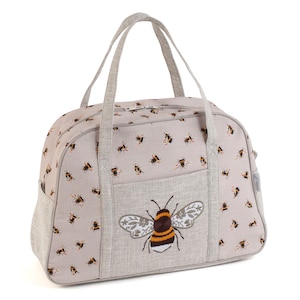 May include: A beige canvas travel bag with a zipper closure and two top handles. The bag has a large embroidered bee on the front and a smaller bee pattern all over.