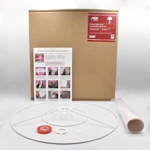 Puede incluir: Un kit para hacer pantallas de lámpara de mesa cónicas. El kit incluye una estructura grande de pantalla blanca, un rollo de material para pantalla, cinta adhesiva de doble cara y una caja de cartón con instrucciones. La caja tiene una etiqueta roja con texto.