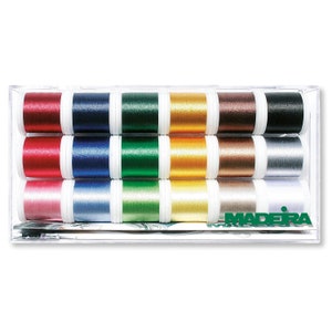 Op de afbeelding: Een doorzichtige plastic doos met 15 spoelen Madeira metallic borduurgaren in verschillende kleuren, waaronder rood, blauw, groen, goud en zilver. De spoelen zijn gerangschikt in drie rijen van vijf.