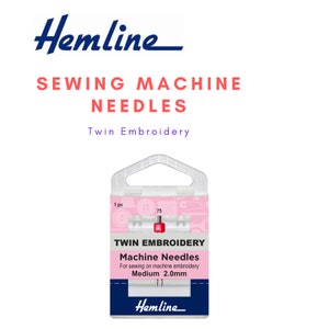 Könnte beinhalten: Eine Packung Hemline Twin Embroidery Nähmaschinennadeln zum Nähen auf der Maschine. Die Verpackung ist rosa und weiß mit dem Text "Twin Embroidery Machine Needles" und "Medium 2.0mm".