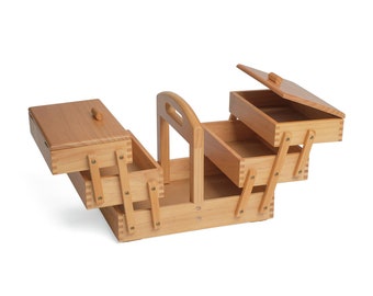 May include: A wooden sewing box with a handle and three drawers. The top drawer is open and the box is angled to show the interior.