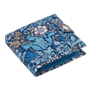 Puede incluir: Una cartera plegada con un estampado floral en tonos azules, beige y rosa. La cartera tiene un cierre de botón a presión y un interior azul suave. El diseño presenta flores y hojas estilizadas.