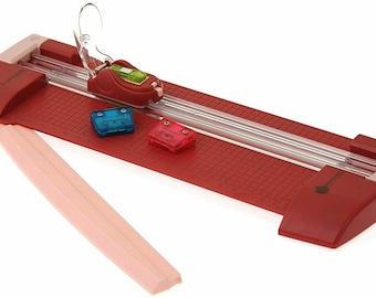 May include: Red paper trimmer with a clear cutting guide and a pink base. It has a built-in ruler and a safety guard. Three small plastic guides are included.
