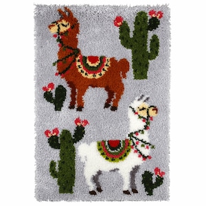 May include: A rug hooking kit featuring two llamas with colorful saddles and floral garlands, standing in front of green cacti with red flowers on a gray background.