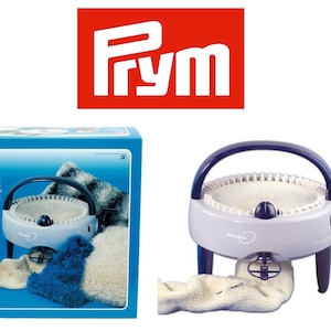 May include: A white and blue Prym Maxi knitting machine with a handle and a crank. The machine is on a white surface and there is a white sock on the machine. The machine is in a box with a blue background and the Prym logo is on the box.