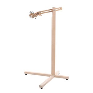Puede incluir: Un soporte de madera clara con un poste vertical sobre una base en forma de cruz. Un brazo horizontal ajustable se extiende desde la parte superior, equipado con un mecanismo de abrazadera metálica asegurado por tuercas de mariposa.