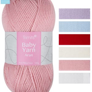 Op de afbeelding: Een bol roze babygaren met een label met de tekst "Trimits Baby Yarn Aran". Het label is roze met witte tekst. Er zijn kleurstalen van garen in lavendel, lichtblauw, rood, wit, roze en wit.