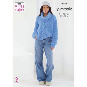 Può includere: Una donna indossa un maglione a trecce blu chiaro con collo a imbuto e jeans blu chiaro. Il maglione ha un aspetto strutturato. Il testo "yumtastic" è visibile, insieme a misure di 81-127 cm.