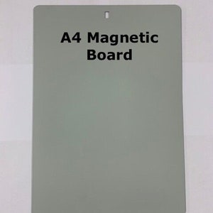 Puede incluir: Pizarra magnética A4 de color verde apagado. La pizarra tiene forma rectangular con esquinas redondeadas y un pequeño agujero en la parte superior para colgarla. El texto "A4 Magnetic Board" está impreso en negro.